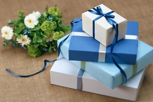 چهار بسته کادو روی هم و یک دسته گل سفید کنار کادوها